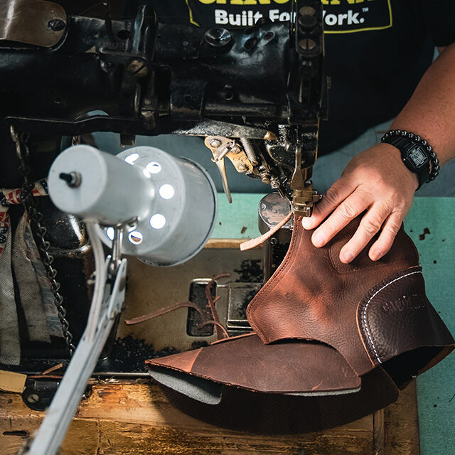 Person in Black Carolina T-shirt sews boot. 