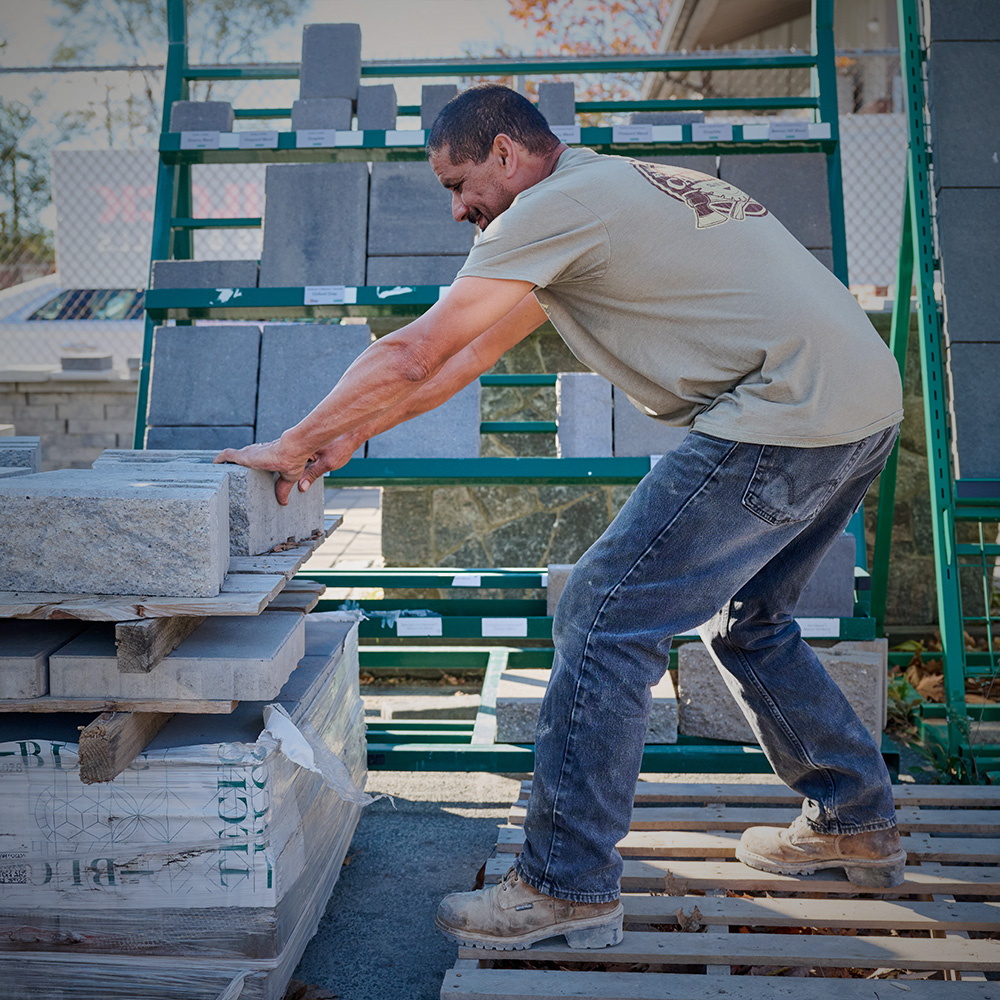 A worker pushing stone blocks and wearing Carolina boots in brown.