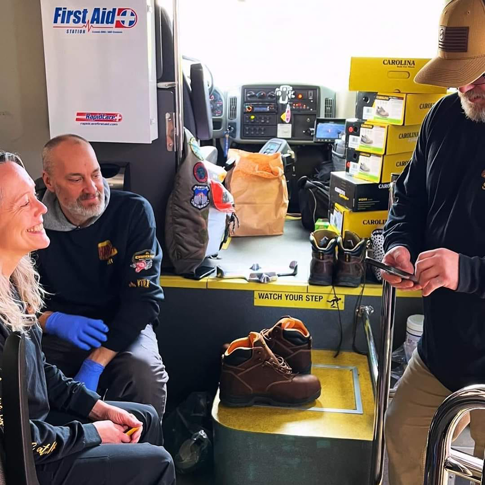 Volunteers sitting in the van with a stack of shoe boxes in the background.